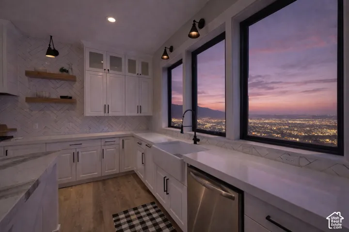 White shaker cabinetry, light-toned countertops, a full height herringbone tile backsplash, and wood-finish flooring