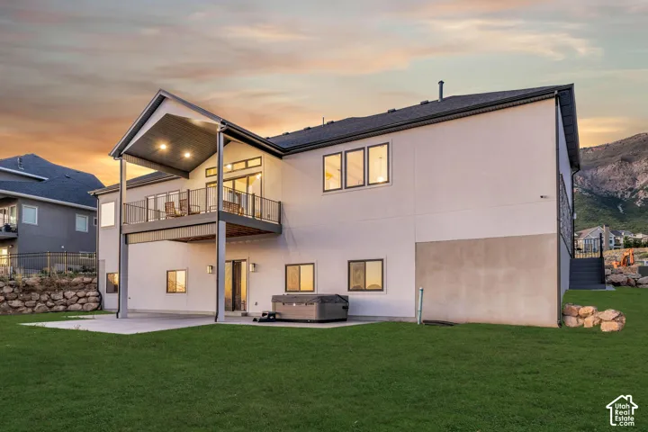 Expansive backyard with a covered patio, upper-level balcony, exterior lighting, and mountain backdrop