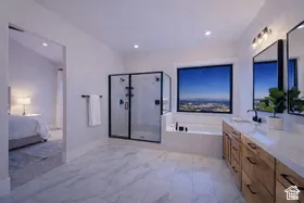 Spacious bathroom featuring marble-look floor tiling, a glass-enclosed shower, built-in soaking tub, dual vanity with wood-finish cabinetry, and a large window