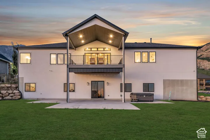 Expansive backyard with a manicured lawn, concrete patio, and upper-level covered balcony