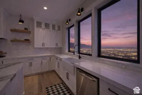 White shaker cabinetry with dark hardware, wood-finish flooring, white countertops, built-in stainless steel dishwasher, and a farmhouse sink