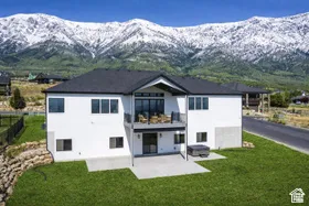 White exterior with a dark roof, featuring multiple windows, an upper-level balcony, and a lower-level patio