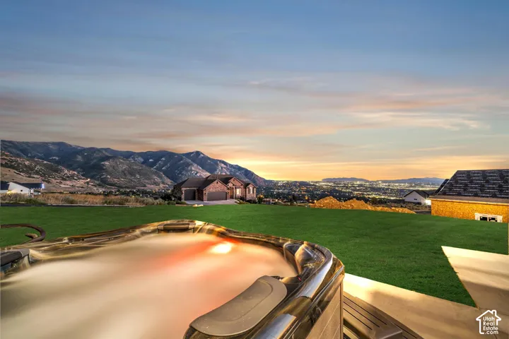 Spacious exterior featuring a built-in spa with integrated lighting, expansive green lawn, and mountain backdrop