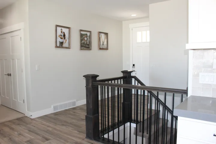 Wood-finish flooring, white paneled doors, dark wood staircase with wrought iron balusters, white cabinetry, and a light-colored countertop