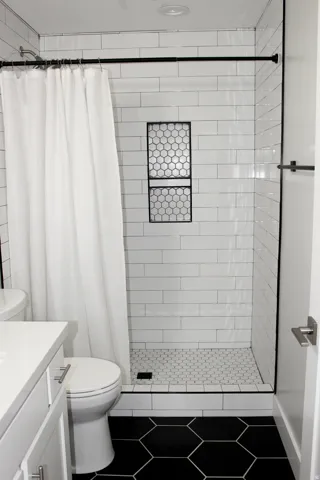 Shower with white subway tile surround, integrated tiled niche, and hexagonal tile shower pan