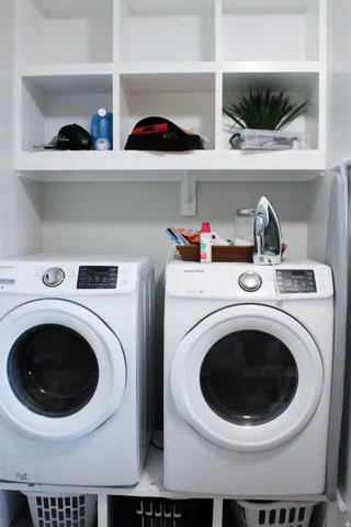 Built-in white storage shelving, white upper wall shelf, and white appliances with dark control panels