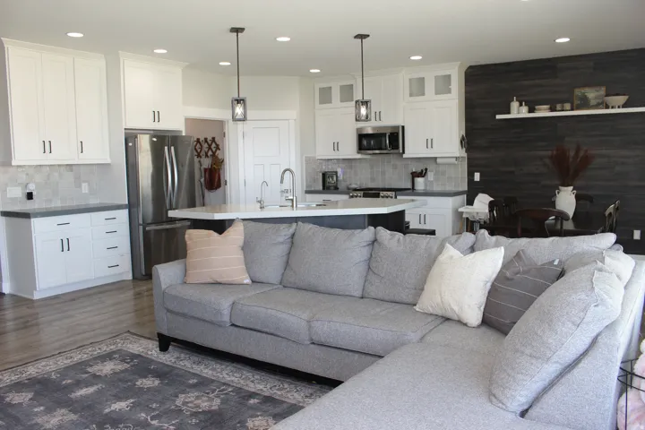 Open-concept living space featuring wood-finish flooring, white cabinetry, integrated stainless steel appliances, a kitchen island with seating, and a dark wood accent wall