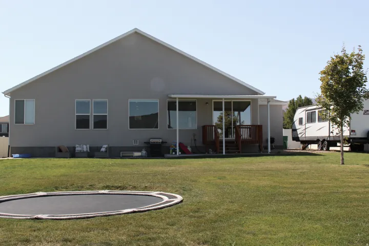 Expansive green lawn, stucco exterior, rear deck with pergola, and multiple windows