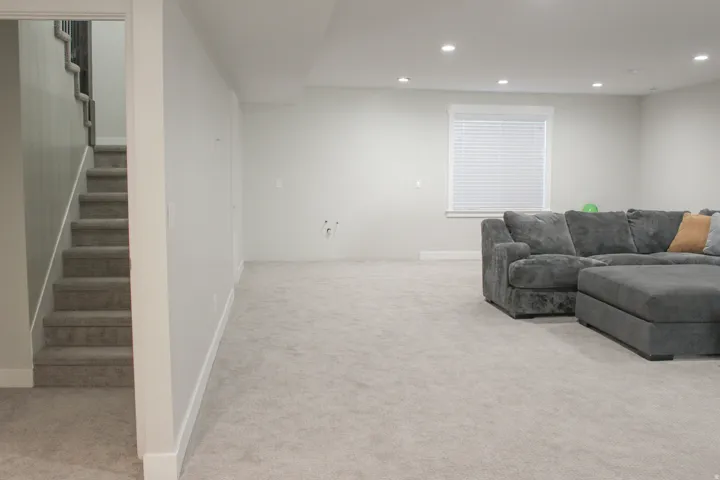 Recessed lighting and a window with horizontal blinds complement the neutral wall tones and light-toned carpeting