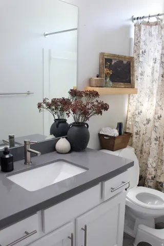 White vanity with shaker-style cabinetry, a gray solid surface countertop, an undermount sink, and a single-handle faucet