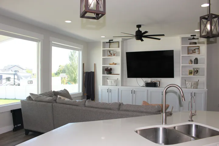 Integrated kitchen and living area featuring a double basin stainless steel sink, a modern gooseneck faucet, custom built-in shelving, a ceiling fan, and recessed lighting