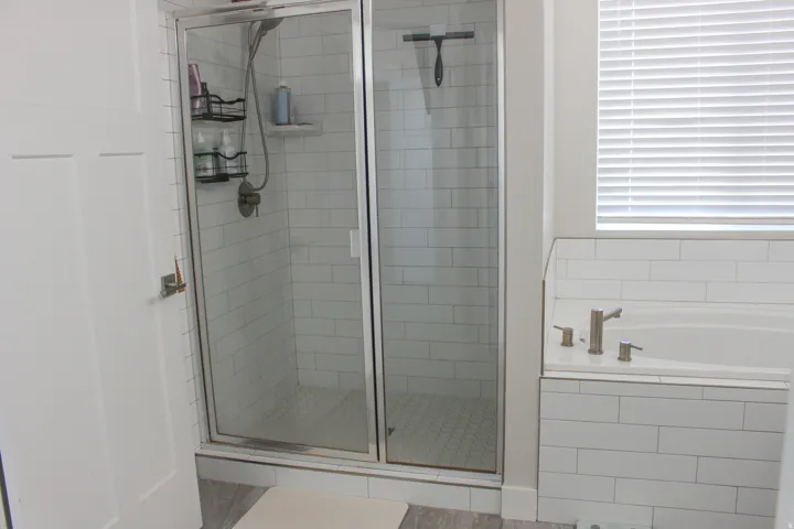 Glass-enclosed shower with subway tile surround, separate built-in bathtub, brushed nickel fixtures, and wood-finish flooring