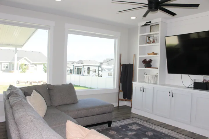 Expansive windows, built-in entertainment center, integrated shelving, modern ceiling fan, and wood-finish flooring