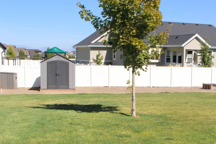 Expansive lawn area with a white privacy fence, detached storage shed, and additional storage bin