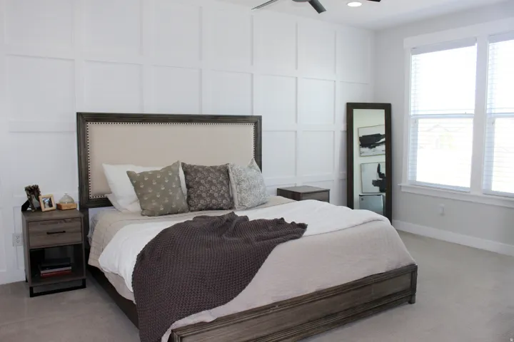 Feature wall with decorative paneling, ceiling fan with integrated lighting, two windows with blinds, and light-toned carpeting