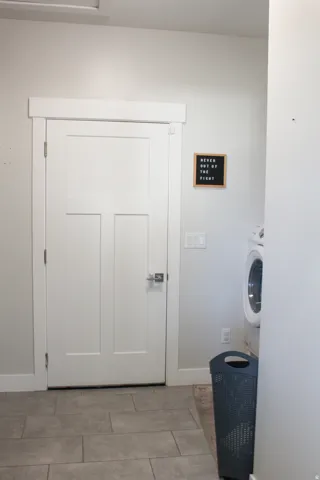 White three-panel interior door with substantial trim, light gray tiled flooring, and a white wall-mounted light switch