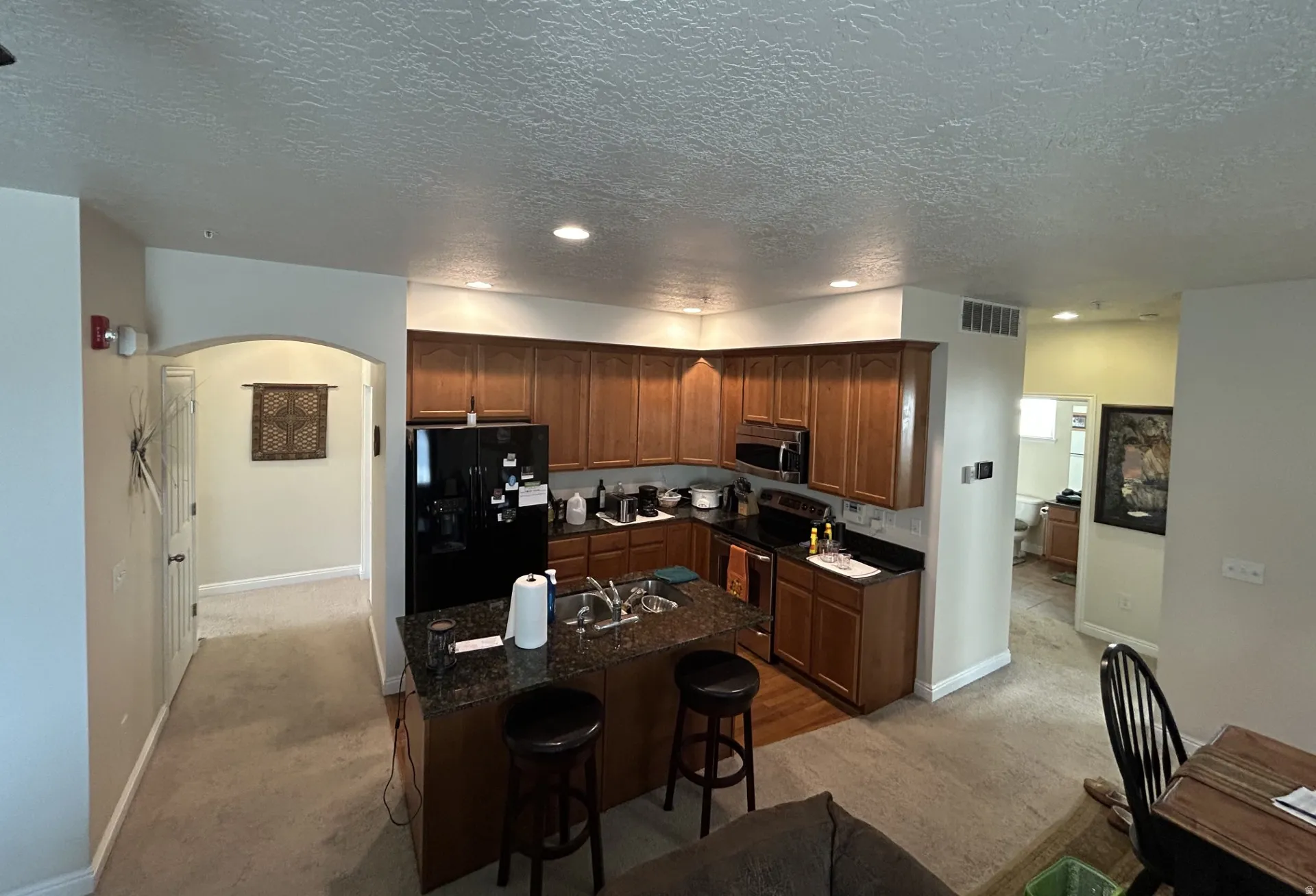 Kitchen featuring wood cabinetry, dark countertops, built-in appliances & a central island with bar seating