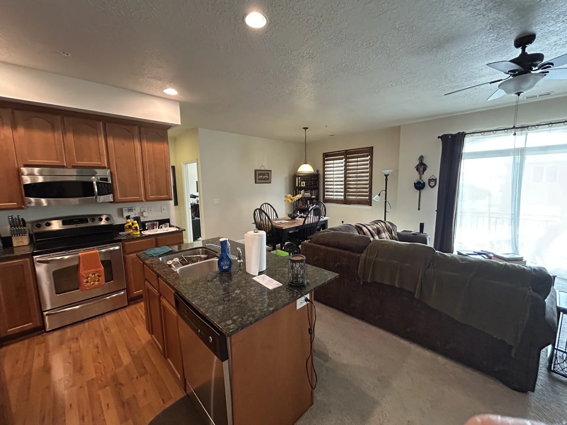 Kitchen featuring wood-finish flooring, stainless steel stove, microwave & a central island with a sink.
