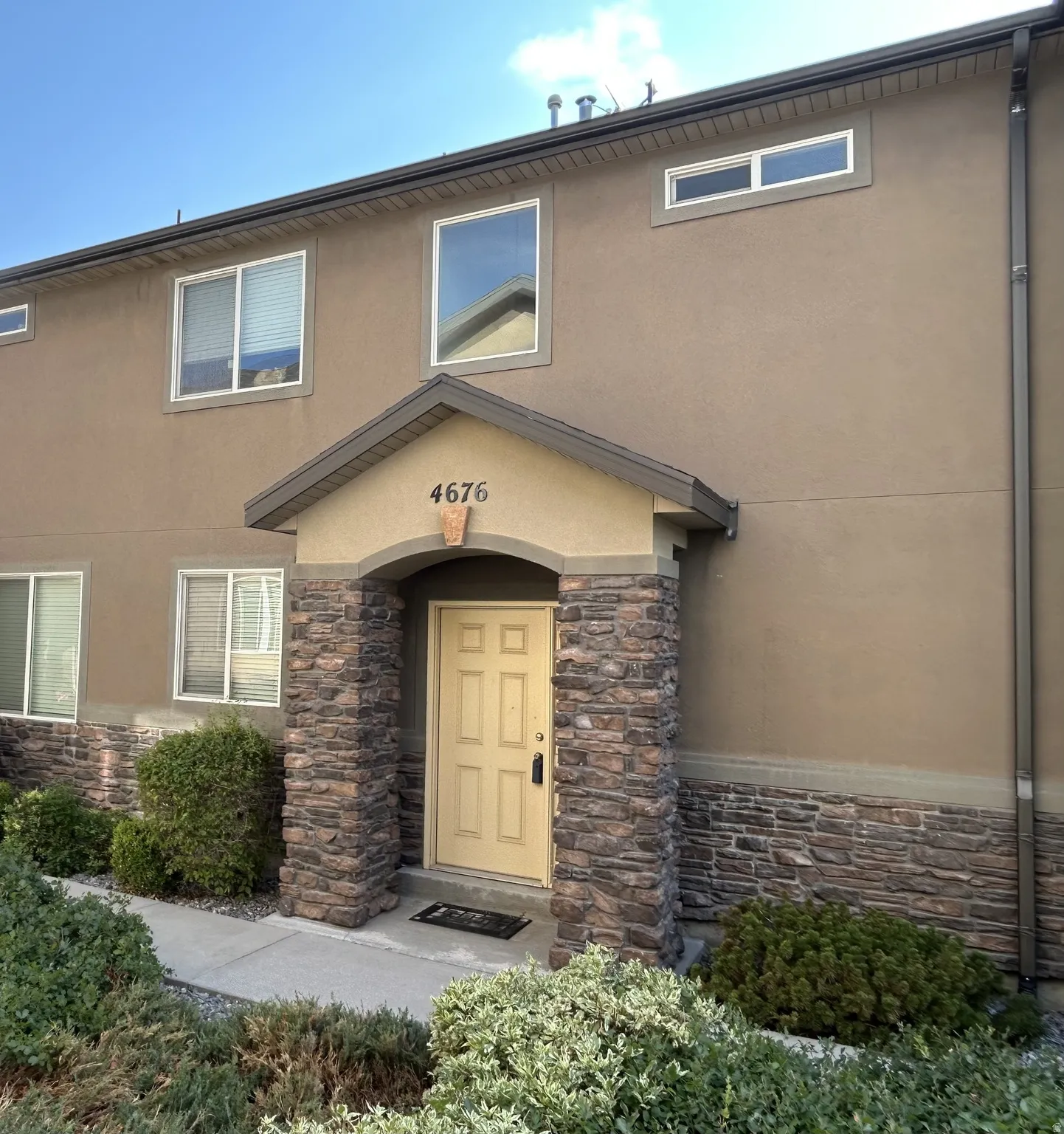 Stone-accented entryway with an arched portico & light-colored door with neutral earth tones.