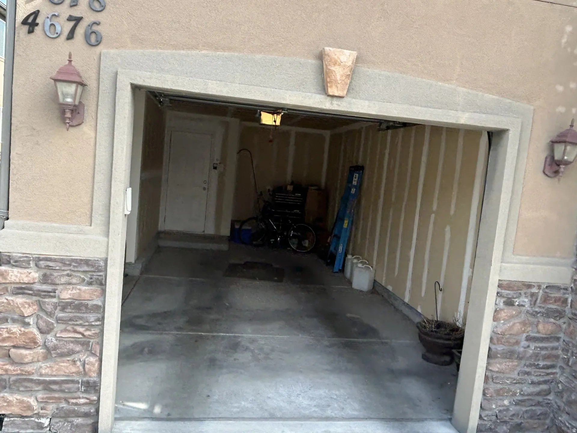 Stucco exterior with stone veneer accents, integrated wall sconces, a built-in garage & a concrete floor.