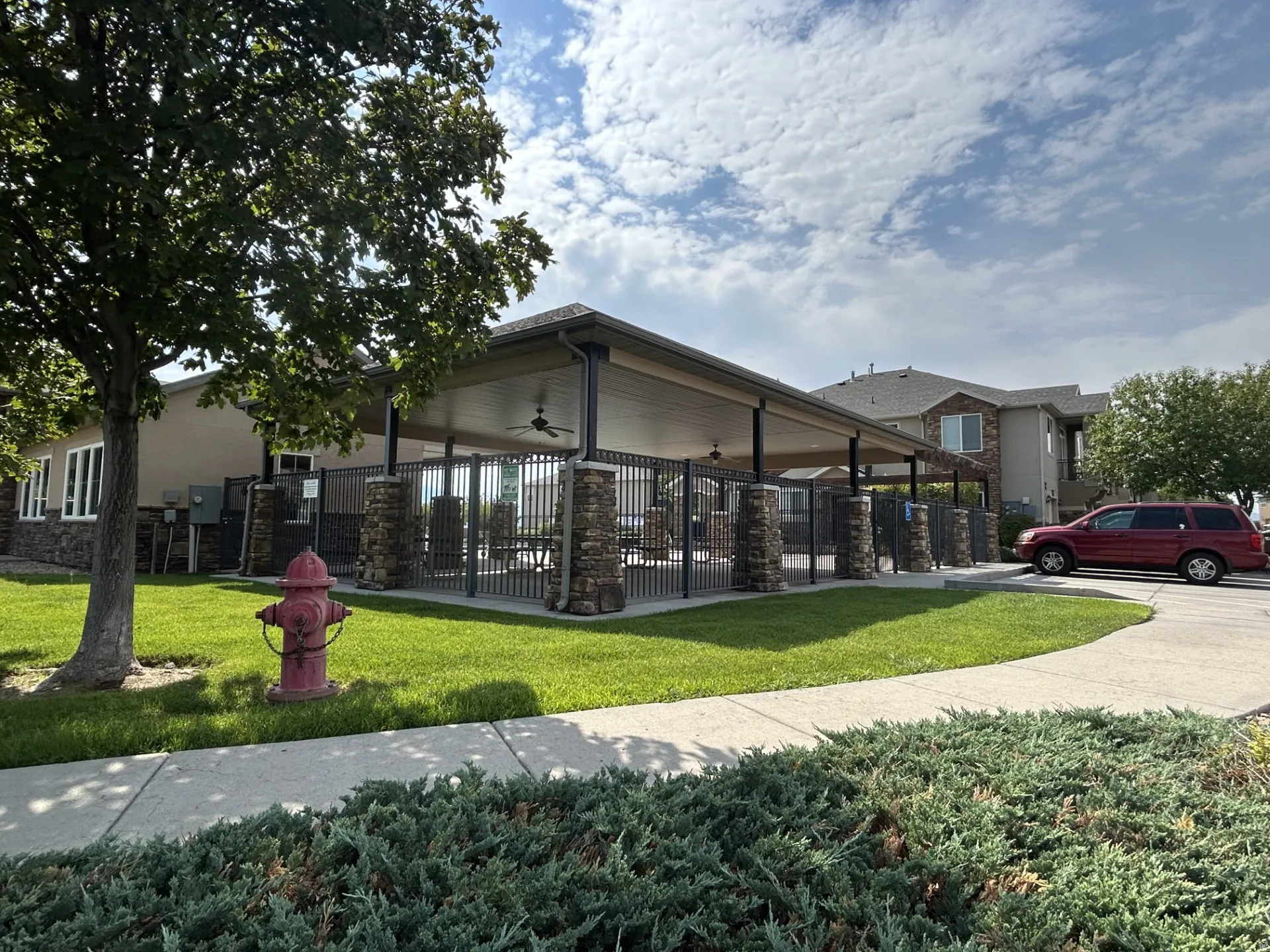 Covered patio structure over picnic area featuring stone-clad pillars, a fenced perimeter & ceiling fans.