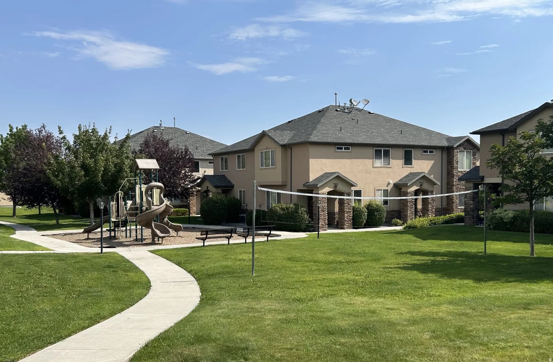 Community green space featuring a playground, manicured lawn, volleyball net & concrete walking paths.