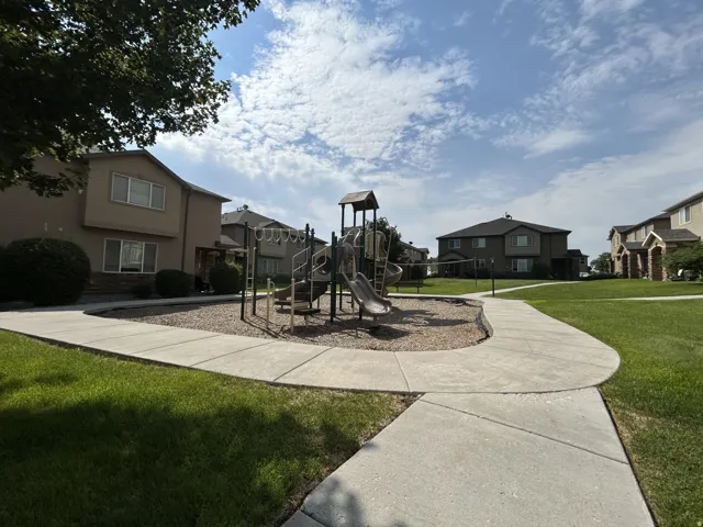 Central playground with a slide with climbing features, surrounded by a concrete pathway & green lawns.
