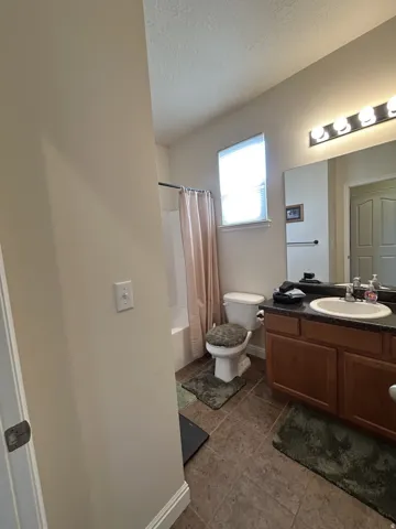 Bathroom featuring a single vanity, integrated sink, wood-finish cabinetry & tiled flooring