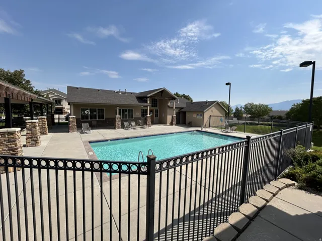 Outdoor swimming pool with surrounding concrete patio, black metal fencing, and an adjacent clubhouse/exercise building featuring stone accents