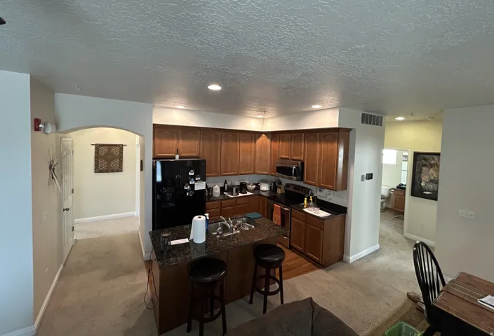 Kitchen featuring wood cabinetry, dark countertops, built-in appliances & a central island with bar seating