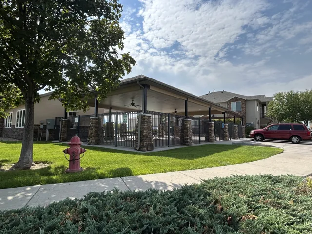 Covered patio structure over picnic area featuring stone-clad pillars, a fenced perimeter & ceiling fans.