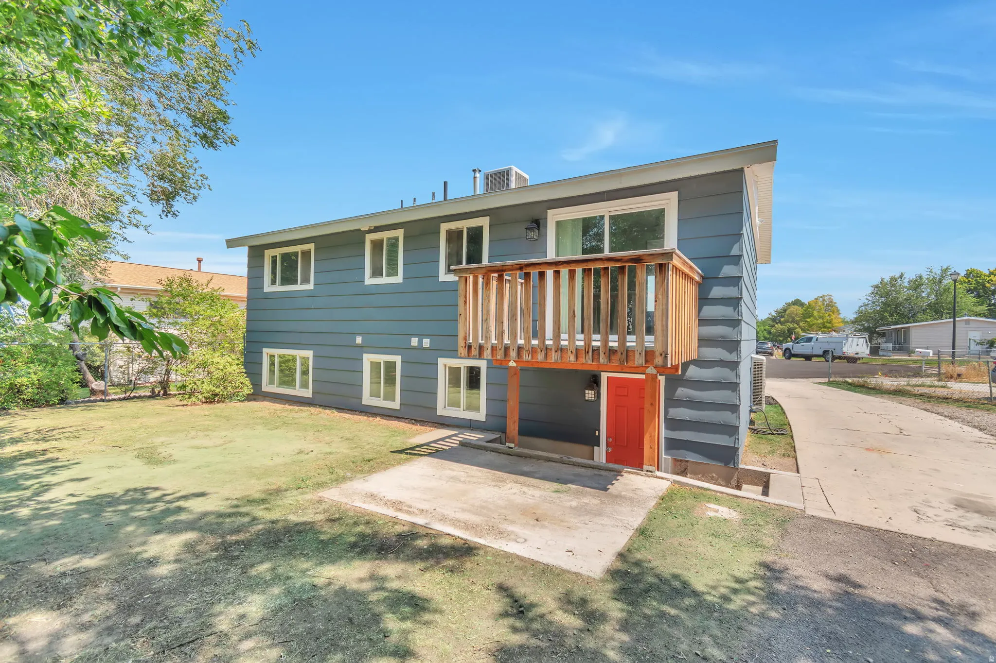 Two-story exterior with horizontal siding, upper-level wood deck, ground-level patio, and a driveway