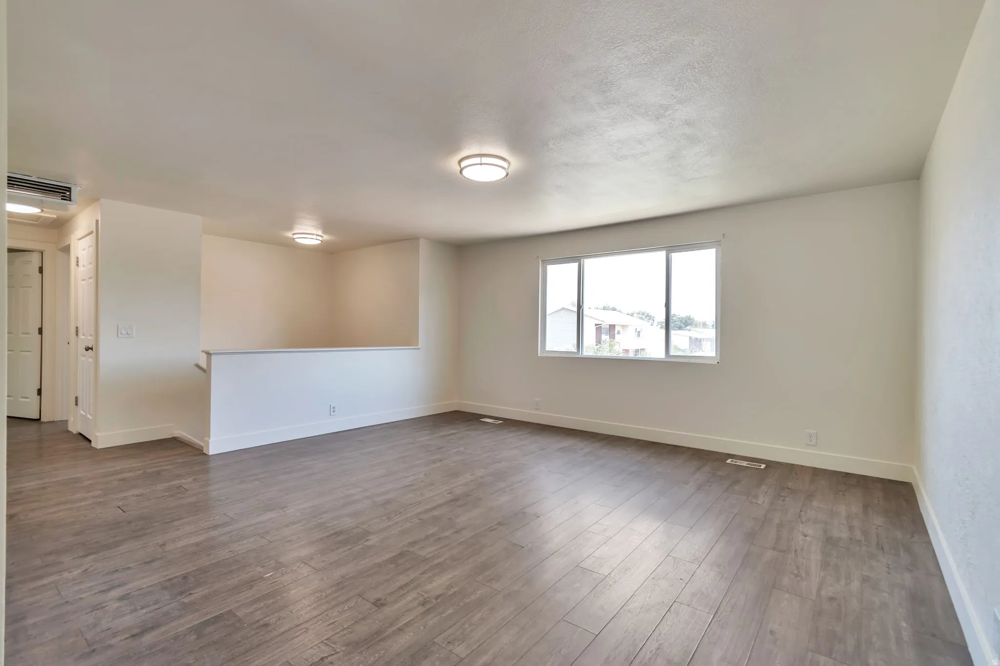 Spacious room featuring wood-finish flooring, white walls, and a large window