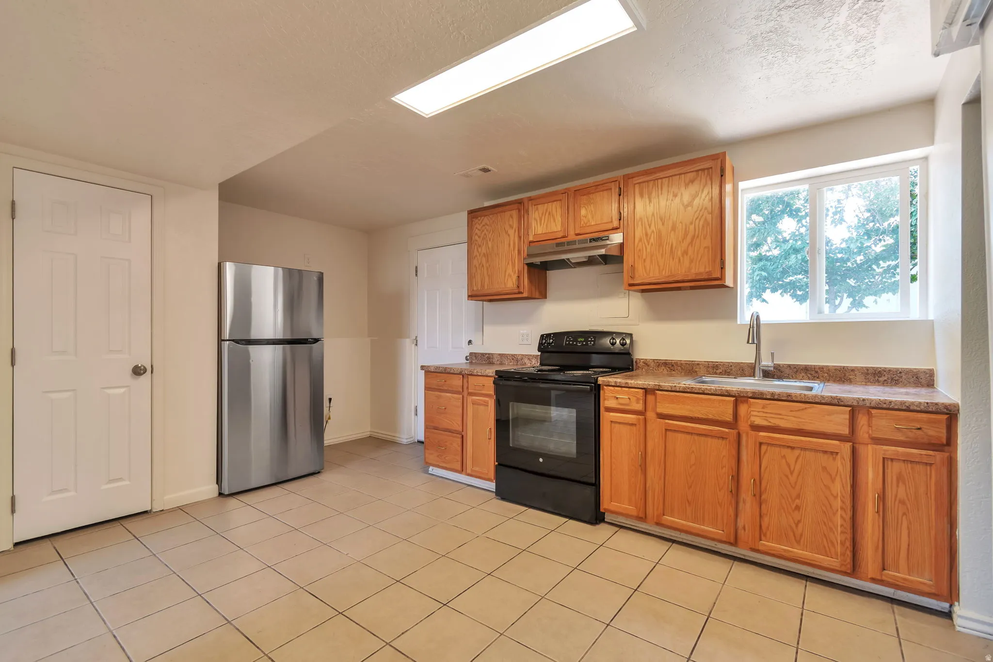 Kitchen featuring wood-finish cabinetry, black appliances, a stainless steel refrigerator, and tiled flooring