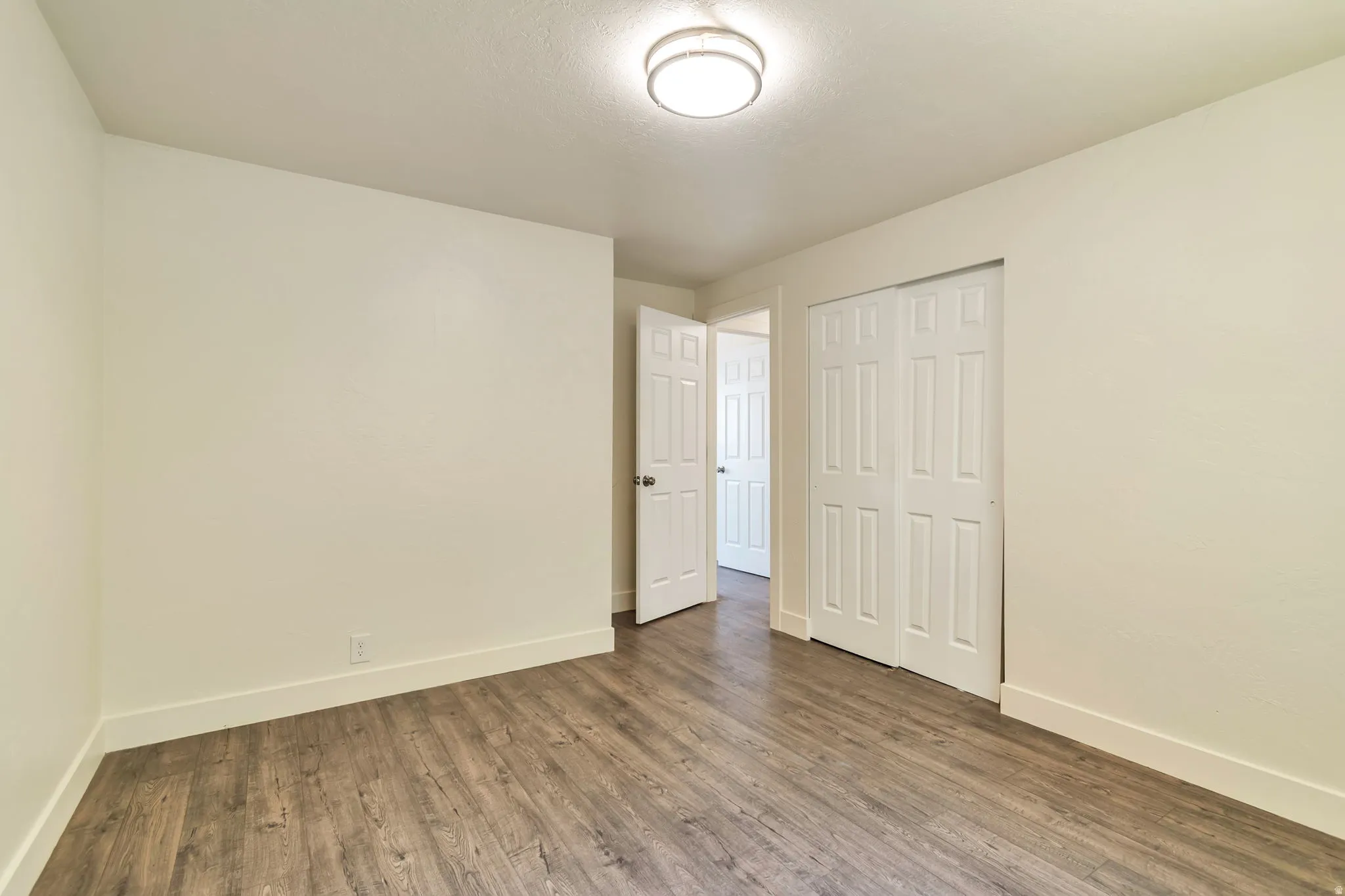 Wood-finish flooring, white walls, white trim, overhead lighting fixture, and a bi-fold closet door