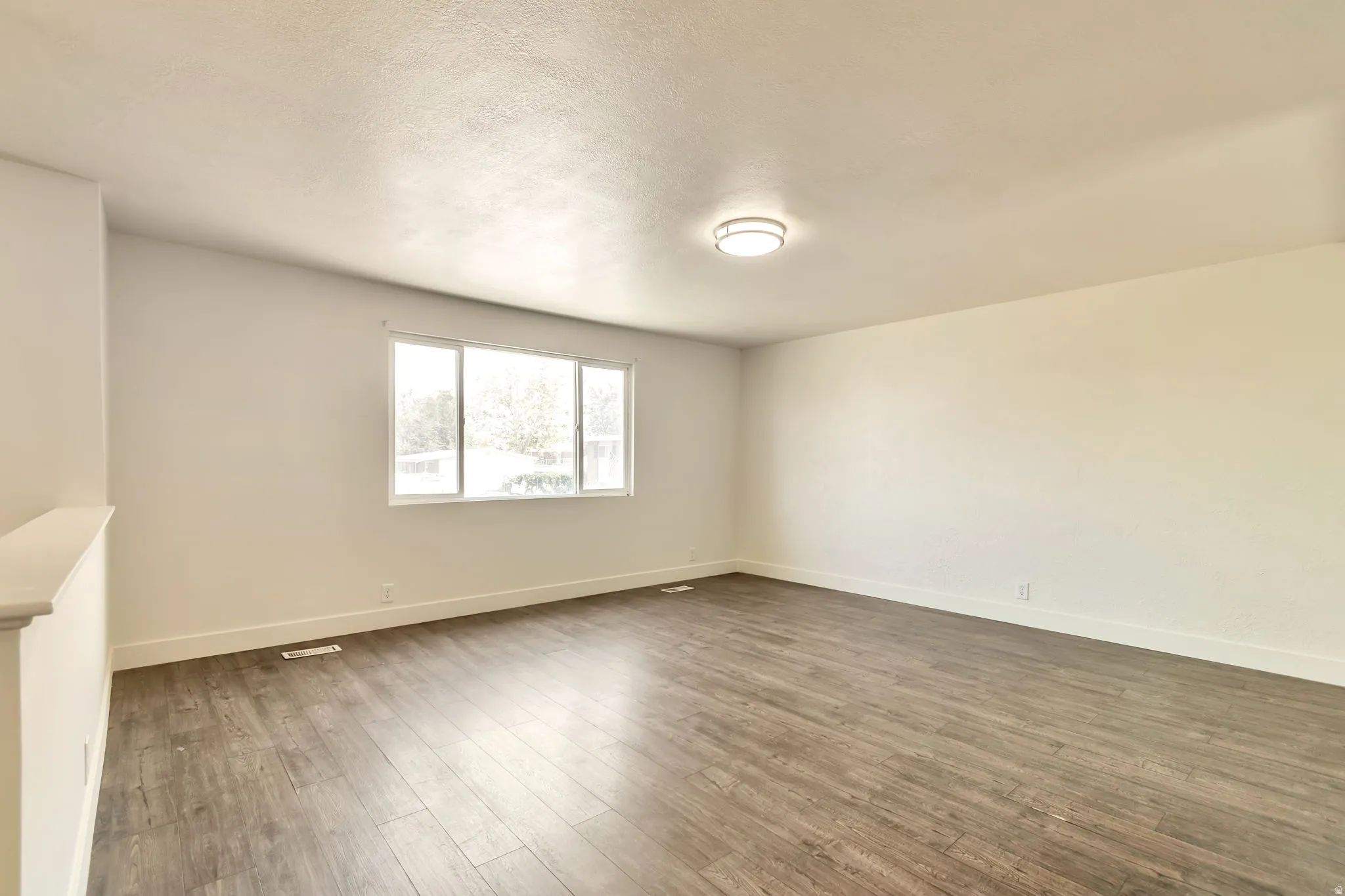 Spacious room featuring wood-finish flooring, white walls, and a large window