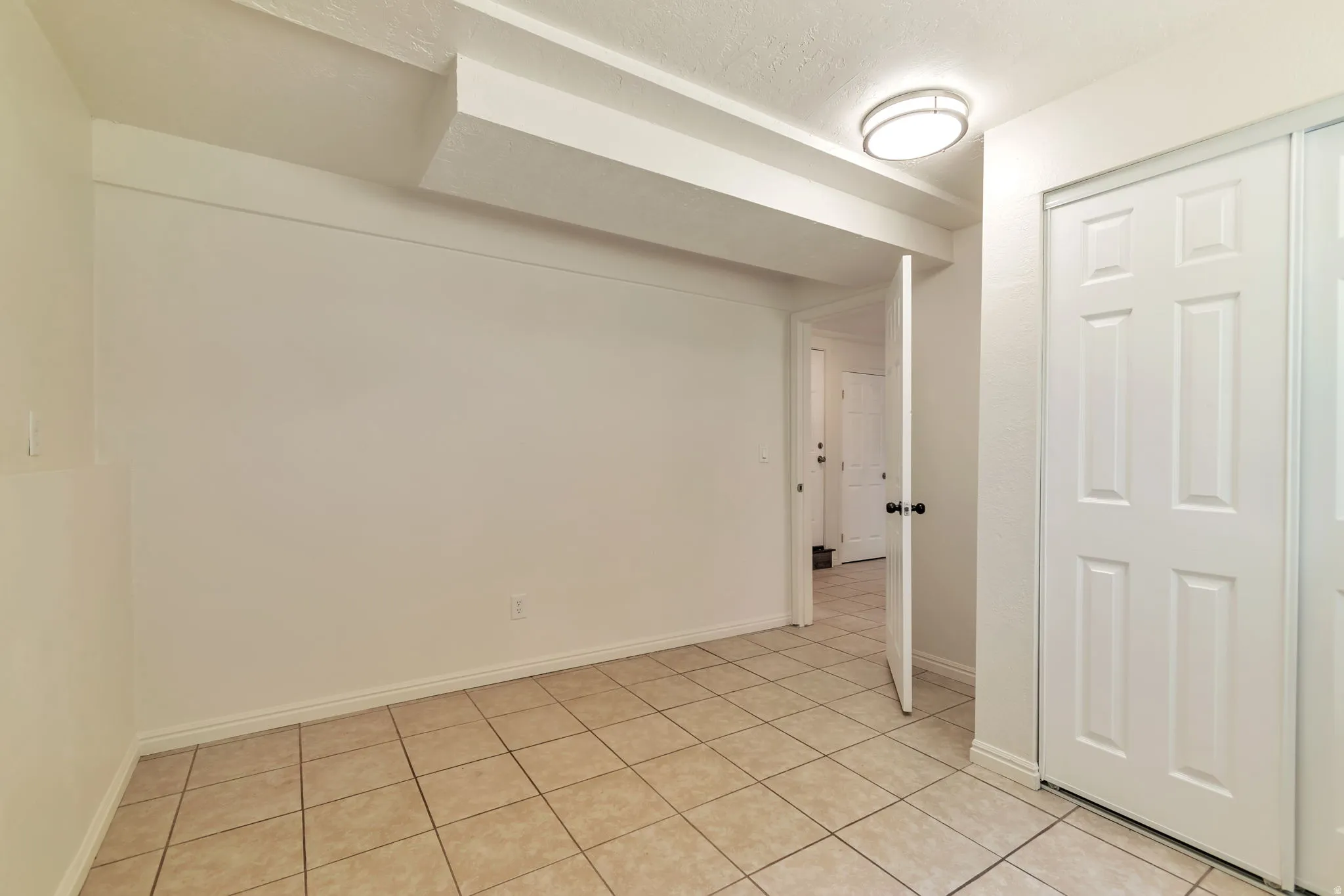 Tile flooring, white walls, overhead lighting, bifold closet doors, and interior door with dark hardware