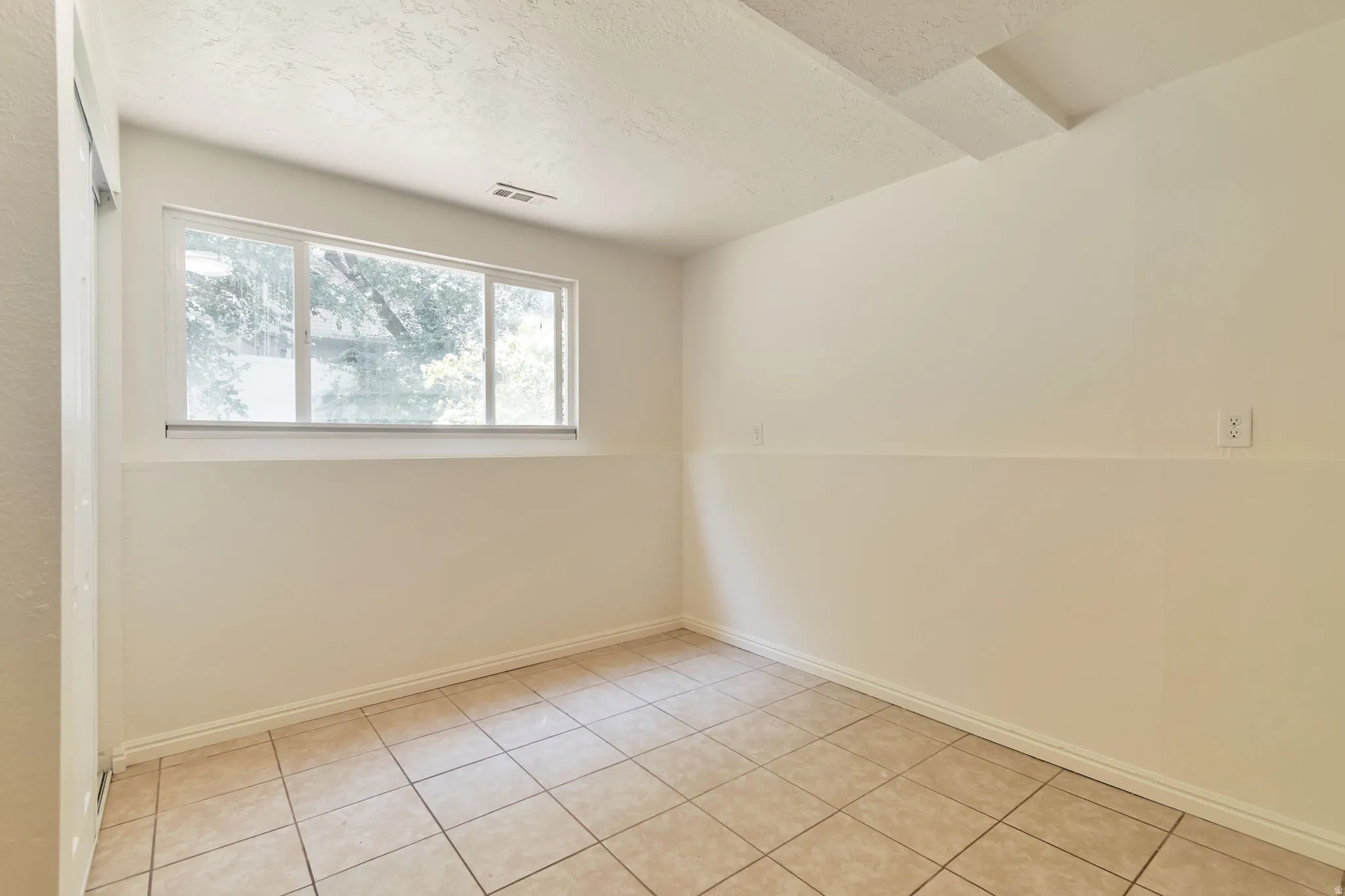 Light-filled room featuring a large window, tiled flooring, textured ceiling, and neutral wall tones