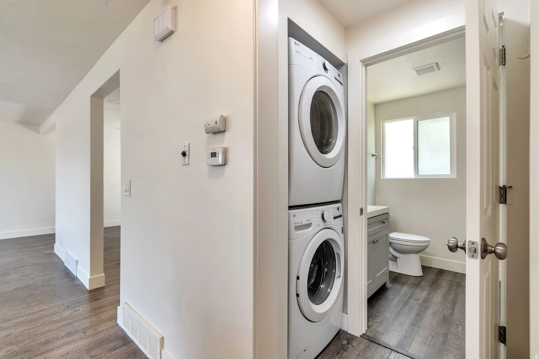 Stackable laundry appliances, wood-finish flooring, and a bathroom with a window