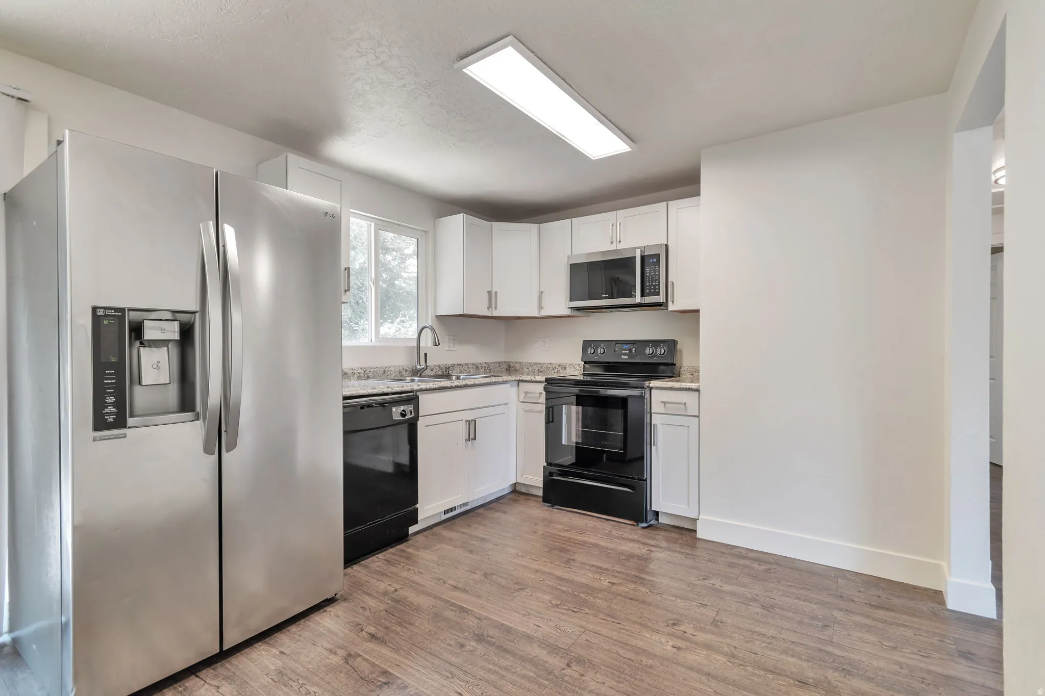 Kitchen featuring wood-finish flooring, white cabinetry, speckled countertops, stainless steel refrigerator, and black appliances