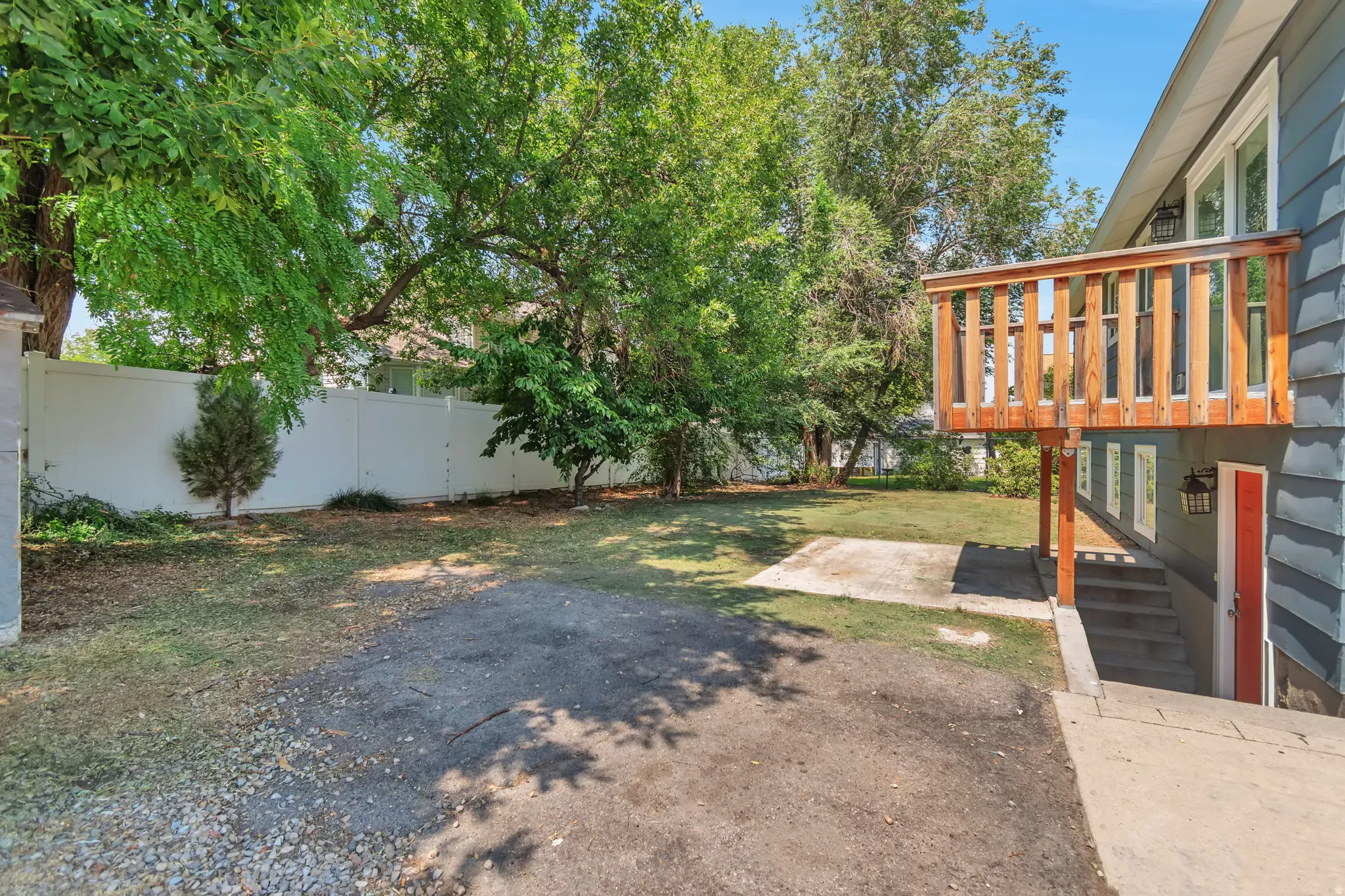 Expansive backyard featuring a privacy fence, mature trees, a deck with wood railing, a concrete patio, and exterior siding
