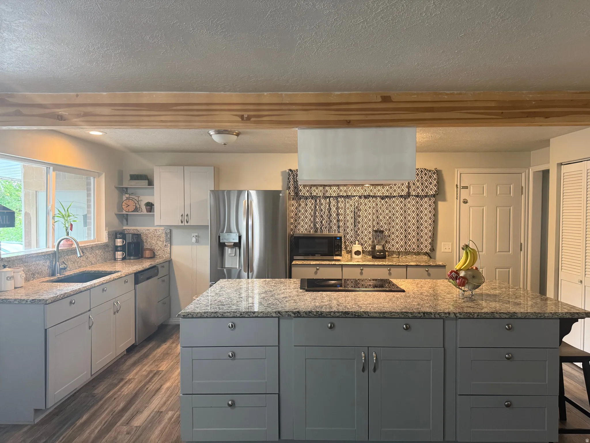 Kitchen featuring wood-finish flooring, granite countertops, gray shaker cabinetry, a center island with an integrated cooktop, and stainless steel appliances
