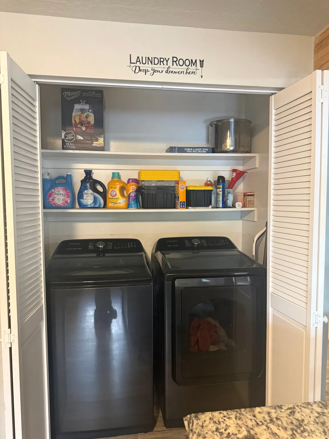 Built-in laundry closet with bi-fold louvered doors, integrated shelving, and dark-finish appliances