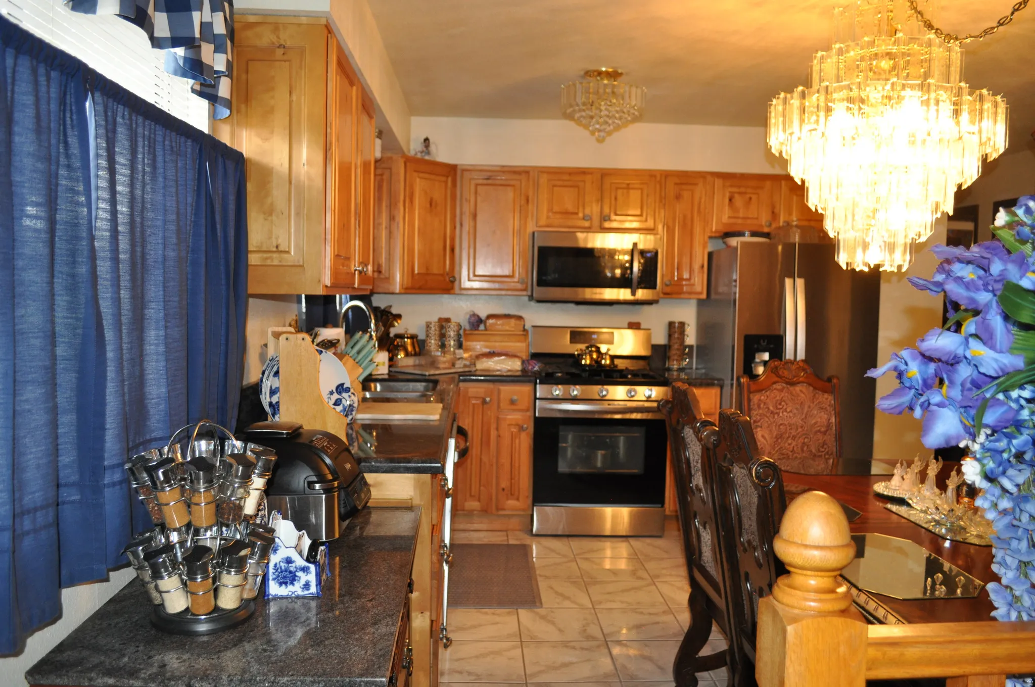 Stainless steel appliances, wood-finish cabinetry, granite-style countertops, tile flooring, and a decorative chandelier