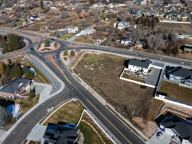 Grassy lot bordering paved roadways, featuring a concrete driveway and adjacent landscaping