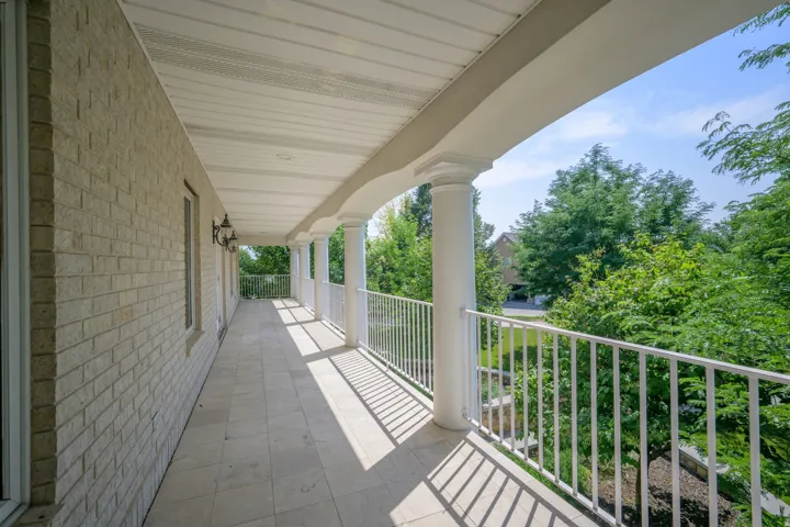 Expansive balcony featuring brick exterior, decorative wall sconces, architectural columns, white railing, and tiled flooring