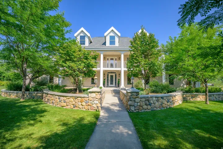 Grand colonial-style residence featuring a prominent portico with columns, a second-story balcony, and dual gabled dormers