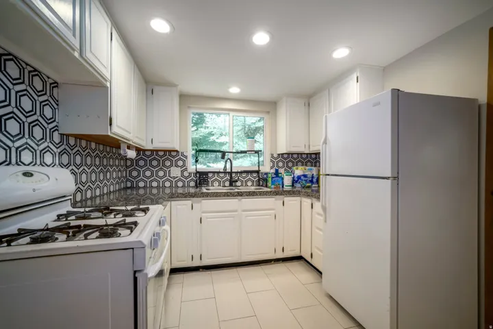White cabinetry with black hardware, hexagonal patterned tile backsplash, dark speckled countertops, and a stainless steel sink with a black-finish faucet