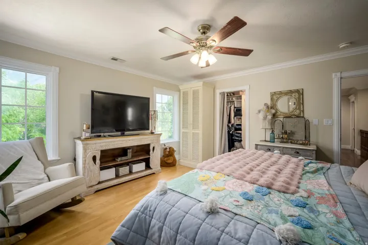 Hardwood flooring, crown molding, built-in open closet with shelving, ceiling fan with integrated lighting, and dual windows