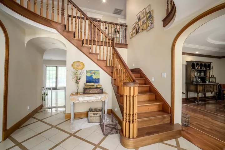 Hardwood staircase with turned balusters, arched doorways, tile flooring with wood-finish inlay, and crown molding